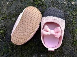 Cute little baby shoes pink and black color on plaster and moss plants background photo