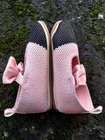 Cute little baby shoes pink and black color on plaster and moss plants background photo