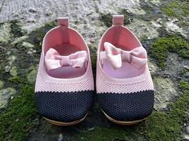 Cute little baby shoes pink and black color on plaster and moss plants background photo