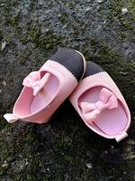 Cute little baby shoes pink and black color on plaster and moss plants background photo