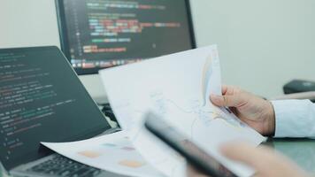 A programmer is holding a piece of paper and a cell phone, possibly working on a project or reading something. The scene suggests a focus on technology and productivity photo