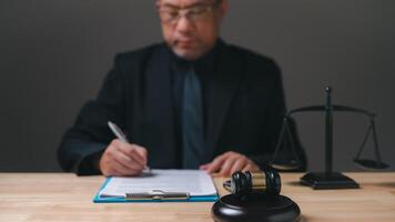 lawyer professional in a suit is writing on a piece of paper. Concept of formality and professionalism, as the man is dressed in a suit and tie and is writing on a desk. The presence of a gavel photo