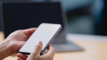 A person is holding a cell phone in their hand, with a laptop in the background. Concept of productivity and focus, as the person is likely working on their phone or laptop photo