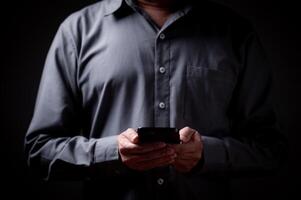 empresario es participación un teléfono inteligente en su mano. él es vistiendo un gris camisa y él es enfocado en su teléfono. concepto comunicación, tecnología, negocio foto