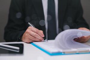 Businessman in a suit is writing with a pen on a piece of paper. Concept of professionalism and formality, as the man is dressed in a suit and tie in office. finance professional approve loan. photo