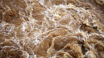 dichtbij omhoog van vuil modderig water met een draaikolk en wit schuim. een rivier- woedend gedurende een flash overstroming. karnen stroomversnellingen Aan een modderig rivier- in overstroming. video