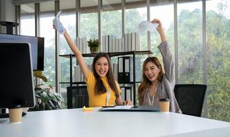 asiático inteligente oficina o mujer de negocios emocionado exitoso negocio gente, celebrando ganar. dos mujer de negocios mirando a un mensual resumen de ventas ese exceder ventas objetivos y lograr rentable crecimiento foto