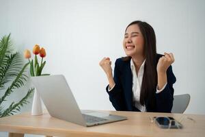 Portrait of a Young attractive Asian woman in a black business suit feeling euphoric celebration online win success achievement result. Success, win, victory, triumph, congratulation, concept. photo