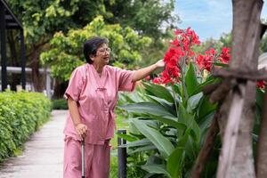 Jubilación mayor antiguo paciente asiático mujer utilizar caña y caminando en hospital al aire libre parque después rehabilitación y el enfermedad tiene curado. sano fuerte médico concepto. foto