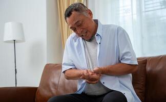 mayor asiático masculino pacientes sufrir desde entumecimiento dolor en manos desde reumatoide artritis. mayor hombres masaje su mano con muñeca dolor. concepto de articulación dolor, reumatoide artritis, y mano problemas. foto