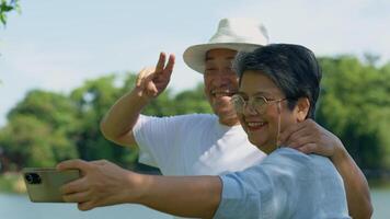 Happy and healthy couples Asian photo and VLOG selfie together for social media in park on leisure. Family and friendship lifestyle, Enjoyment of active seniors, and outdoor activity after retirement