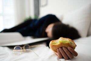 ocupado y cansado mujer de negocios comiendo un pan para desayuno en cama a hogar y trabajando a entregar financiero declaraciones a un jefe. sobrecargado de trabajo y insalubre para Listo comidas, agotamiento concepto. foto