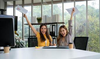 asiático inteligente oficina o mujer de negocios emocionado exitoso negocio gente, celebrando ganar. dos mujer de negocios mirando a un mensual resumen de ventas ese exceder ventas objetivos y lograr rentable crecimiento foto