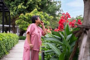 Jubilación mayor antiguo paciente asiático mujer utilizar caña y caminando en hospital al aire libre parque después rehabilitación y el enfermedad tiene curado. sano fuerte médico concepto. foto