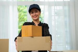 Smiling young woman holding cardboard box, Online shopping delivery concept. Online marketing and delivery. Young asian girl holding and carrying brown boxes for shipping to the client. photo