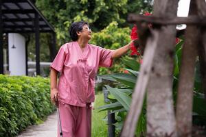 Jubilación mayor antiguo paciente asiático mujer utilizar caña y caminando en hospital al aire libre parque después rehabilitación y el enfermedad tiene curado. sano fuerte médico concepto. foto