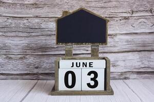 Chalkboard with June 03 date on white cube block on wooden table. photo