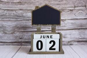 Chalkboard with June 02 date on white cube block on wooden table. photo