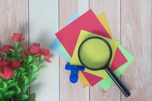 Colorful adhesive paper with magnifying glass on wooden desk. photo