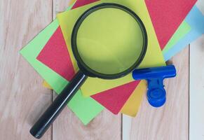 Colorful adhesive paper with magnifying glass on wooden desk. photo