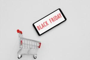 Shopping cart with a smartphone and text Black Friday on the screen on a grey background. photo