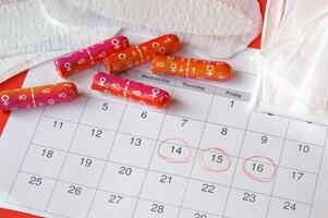 Menstrual pads and tampons on menstruation period calendar with on red background. photo