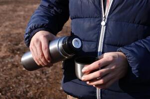 Man's hands pouring fresh hot cocoa from thermos to cup. photo