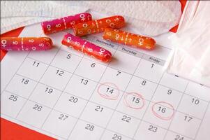 Menstrual pads and tampons on menstruation period calendar with on red background. photo