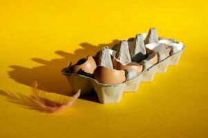 Background view broken of brown chicken eggs in an open egg carton isolated on yellow. photo