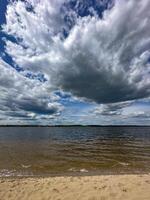Majestic clouds loom over a serene lake with gentle waves and a sandy shore, creating a tranquil yet powerful natural scene photo