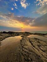 Warm sunset over tranquil beach with textured rocks and reflective tide pools, serene nature scene photo