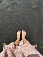 Bare feet stepping onto the unique, volcanic black sand of a beach, providing a natural and earthy point-of-view experience photo