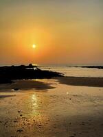 Warm sunset over tranquil beach with textured rocks and reflective tide pools, serene nature scene photo