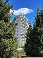 A high-rise building towers over lush green trees on a clear sunny day, showcasing the contrast between nature and urban development photo