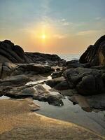 Warm sunset over tranquil beach with textured rocks and reflective tide pools, serene nature scene photo
