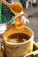 A woman pours honey from a barrel into a glass jar photo