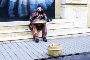 bakú, azerbaiyán - diciembre 02, 2023 . un joven chico con rastas y un barba obras de teatro un percusión musical instrumento colgar en el ciudad en el calle. foto