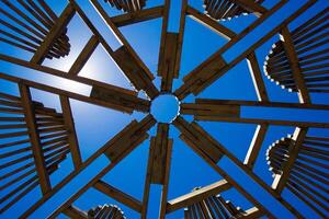 architectural wooden structure with a complex pattern of intersecting beams that frame the sky above photo