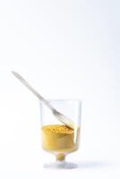 Colorful yellow holi powder sand in a glass cup with wooden spoon on white background. photo