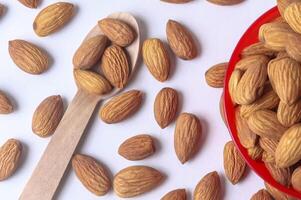 Close-up shot of almonds in a red bowl and wooden spoon isolated on white background. photo