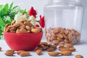 Almond in a red bowl on a white background with flowers. Healthy food. photo