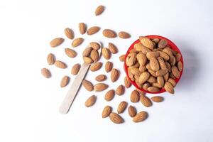 Almonds in a red bowl and wooden spoon isolated on white background. photo