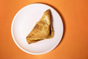 Veg puff pastry on a white plate on a bright orange background. Top view photo