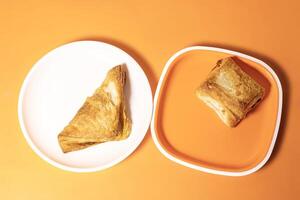 Two different types of crunchy veg puff pieces on a plate on an orange background photo