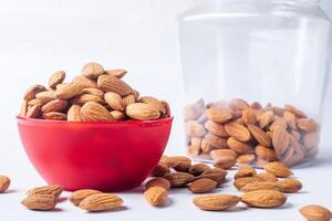 Almonds in red bowl on white background with clear glass jar. closeup photo