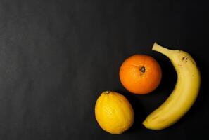 Orange, lemon and banana on black background. photo