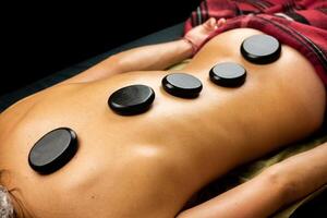 Black hot basalt stones are laid out on a woman's back. Massage procedure. Therapist relieves stress from client's sore spots. Spa treatments. photo