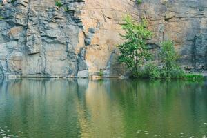 Stone rock on the shore of the lake. Flooded granite quarry. Consequences of impact on nature and ecology. Anthropogenic influence. photo