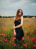 Beautiful young girl in a black evening dress posing against a poppy field on a cloudy summer day. Portrait of a female model outdoors. Rainy weather. Gray clouds. photo