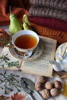 Cozy autumn composition with cup of tea book walnuts and fruits photo
